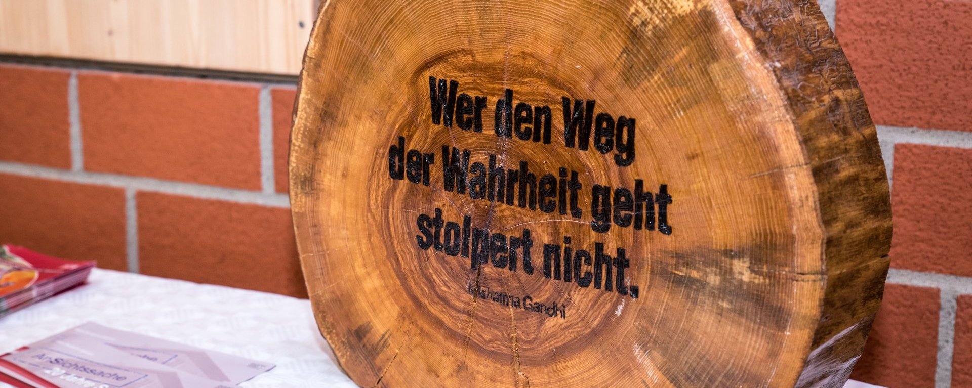 Holzstamm-Scheibe mit eingebranntem Spruch: "Wer den Weg der Wahrheit geht stolpert nicht - Mahetma Gandhi"