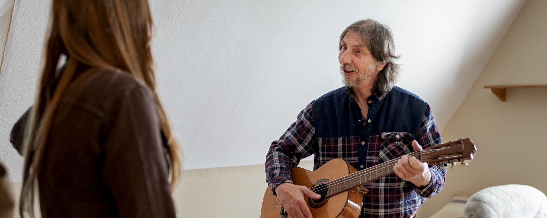 Eine Person spielt einer anderen Person etwas auf der Gitarre vor. 