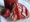 Ein Glas mit roter Marmelade steht neben einem Stück Brot, das dick mit der Marmelade bestrichen ist. Daneben liegt eine frische Erdbeere auf einem weißen Tuch.
