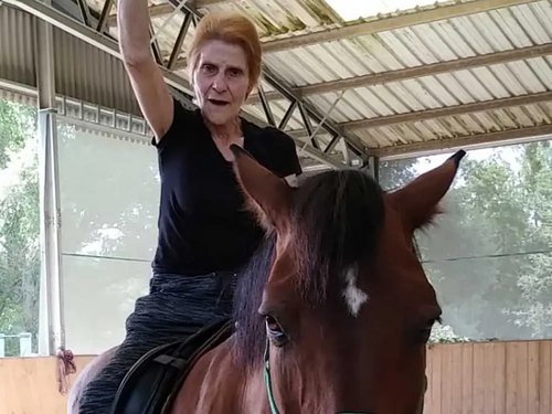 ältere Frau auf einem Pferd streckt eine Hand in die Luft