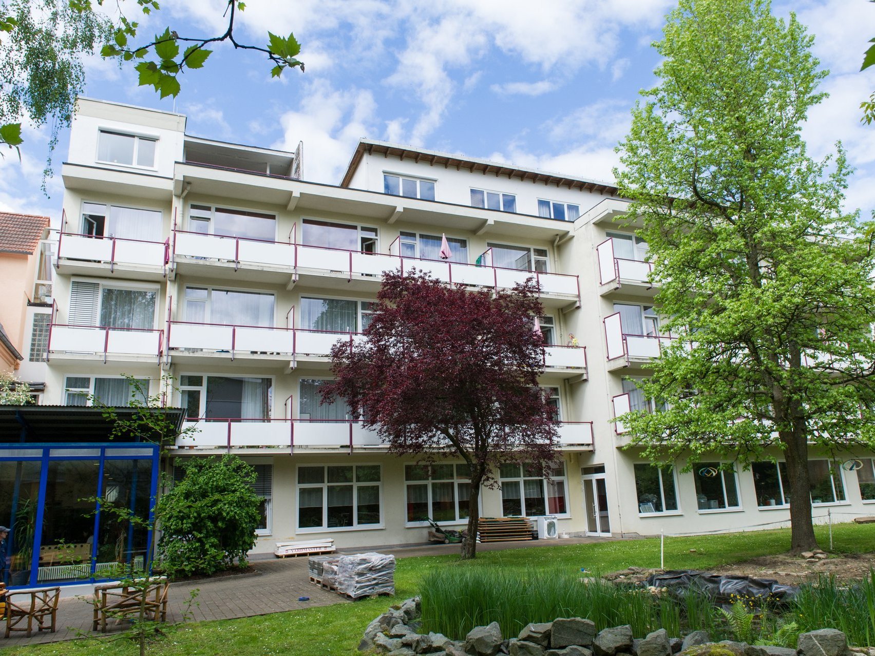 Aussenansichtvon Haus Noah - Das kubistische Haus hat viele abgetrennte Balkone und davor ist ein kleiner Teich und Bäume zu sehen