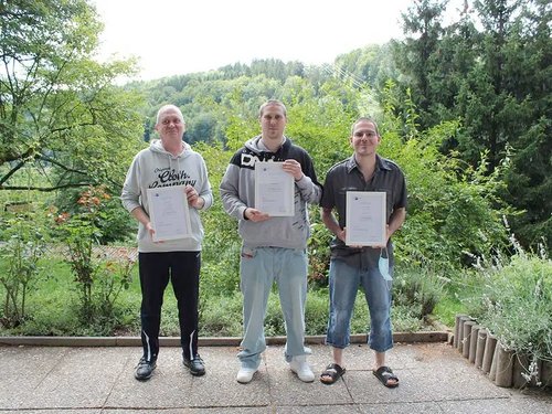 drei junge Männer, die eine Auszeichnung in den Händen Halten - auf einer Terrasse, im Hintergrund Bäume