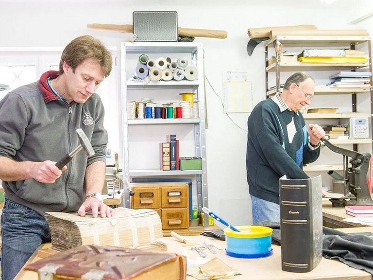Werkstatt: Zwei Männer arbeiten als Buchbinder und restaurieren ein altes Werk 