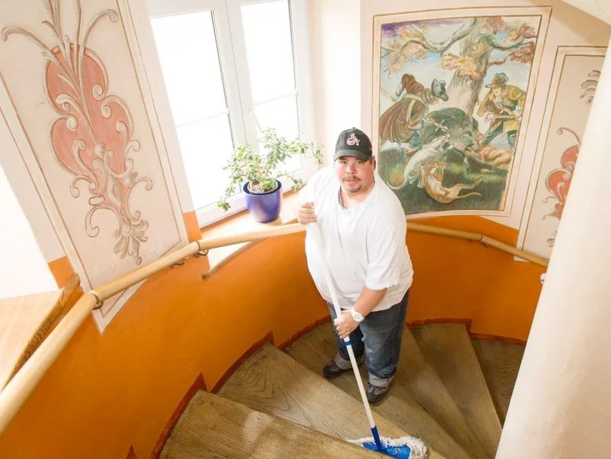 Ein Mann mit Base-Cap und weissem T-Shirt wischt die Treppenstufen im Haus