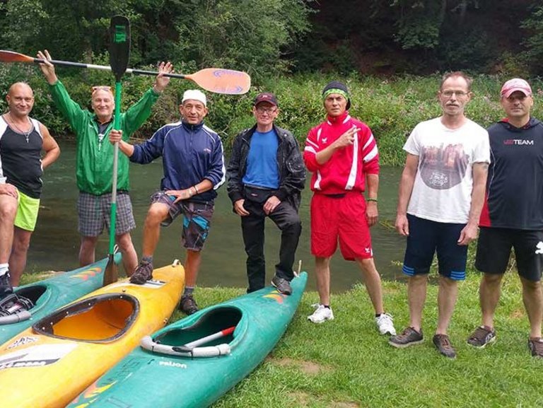 Eine Gruppe Männer stehen hinter ihren Kajaks. Zwei von ihnen halten ein Paddel in den Händen.