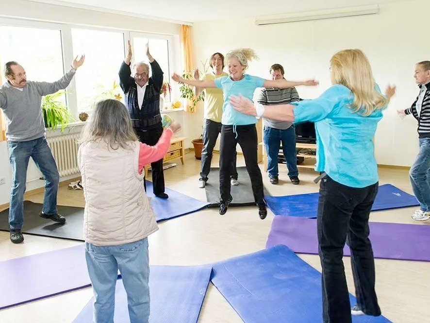 Eine Gruppe Fauen und Männer stehe auf Yoga-Matten und machen diverse Übungen