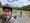 Ein Mann mit Helm und Brille macht ein Selfie, während ein kleiner Hund aus dem Helm schaut. Im Hintergrund fährt eine weitere Person auf einem Fahrrad auf einem asphaltierten Weg.