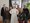 Sechs Personen posieren für ein Gruppenfoto mit einer lebensgroßen Pappfigur von Papst Johannes Paul II. Im Hintergrund ist eine schwarz-weiße Flagge mit einem Kreuzsymbol an der Wand zu sehen.