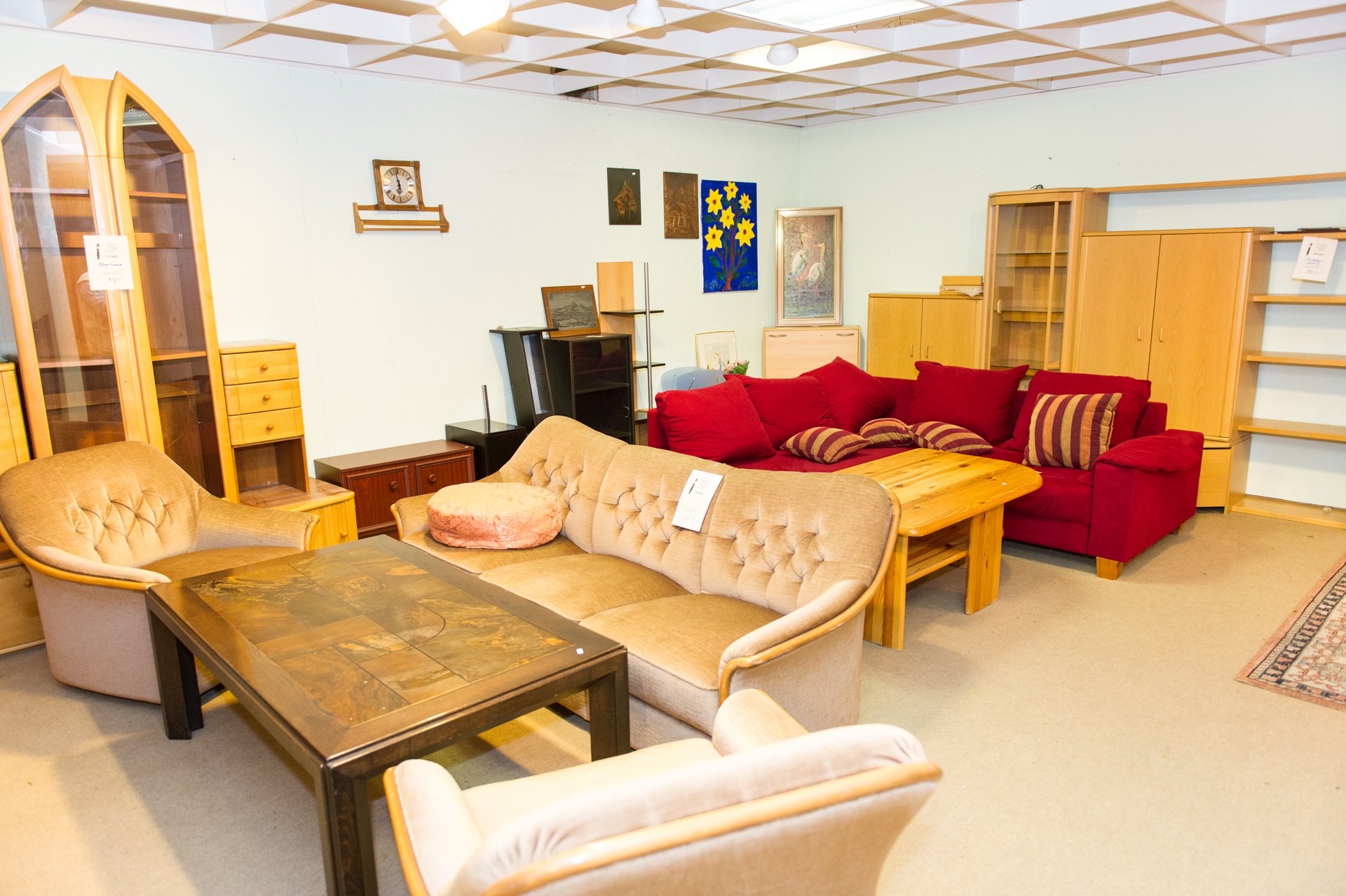 Ausstellungsraum: zwei Sofas, Sessel, Tische, Schränke und einige Bilder stehen im Raum oder hängen an der Wand